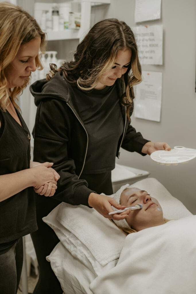 Student learning from a teacher how to do a facial on a client.